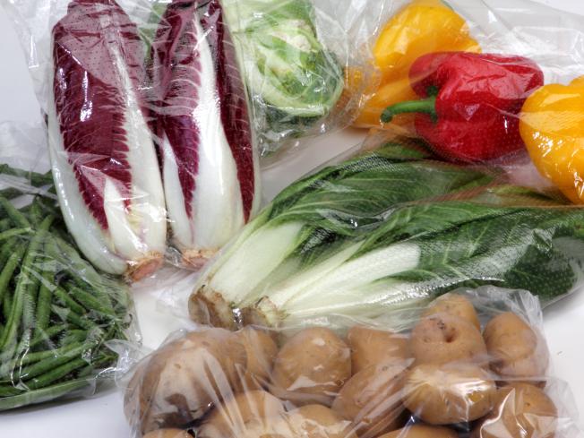 A picture of various vegetables in plastic bags against a white background